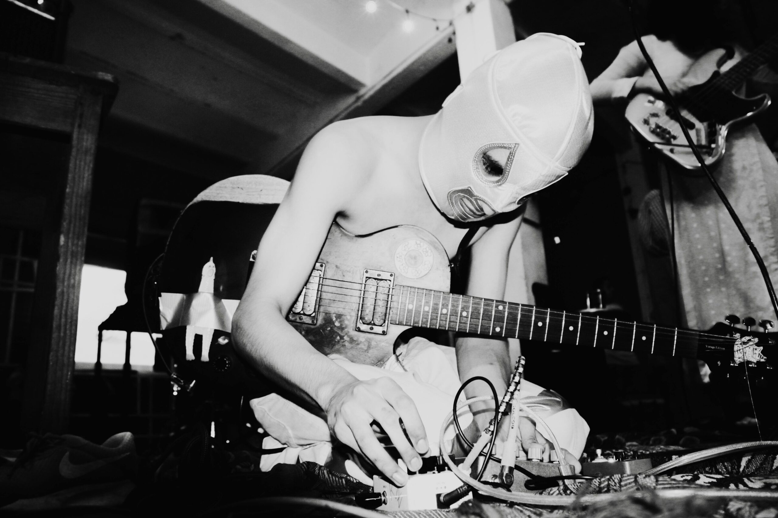 Artsy black and white photo of a masked musician adjusting guitar effects during a live performance.