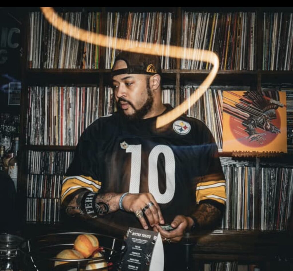 Bartender, Vick, standing behind the bar in front of vinyl library